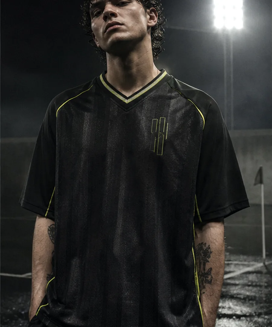 Temporary product image for Drop 02, a fictional black football shirt under night floodlights.